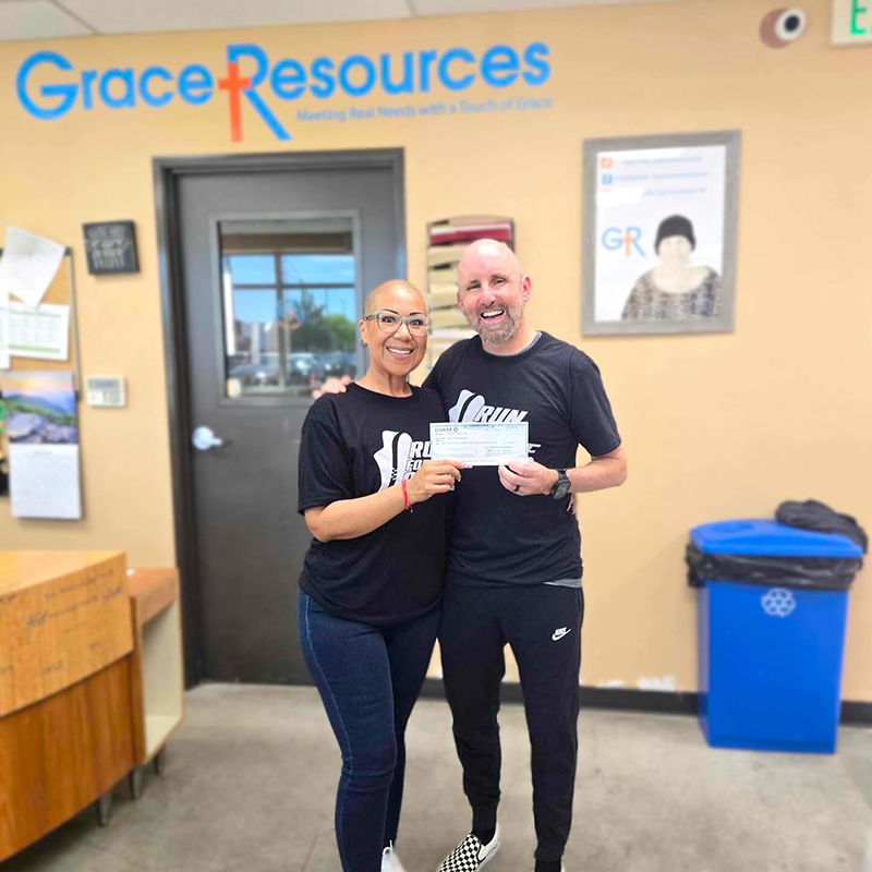 Two hands exchange a takeout container at a community event, surrounded by people and food containers in the background.