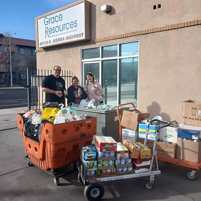 A group of people in a warehouse, stacking boxes and organizing items among racks of clothing. The atmosphere is busy and collaborative.