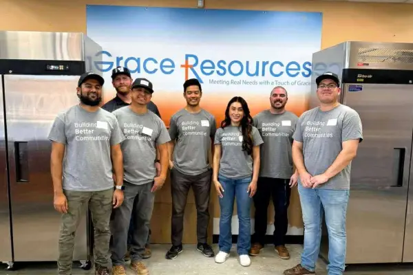 A diverse group of six individuals wearing matching t-shirts that read "Building Better Communities" stands in front of a branded backdrop.